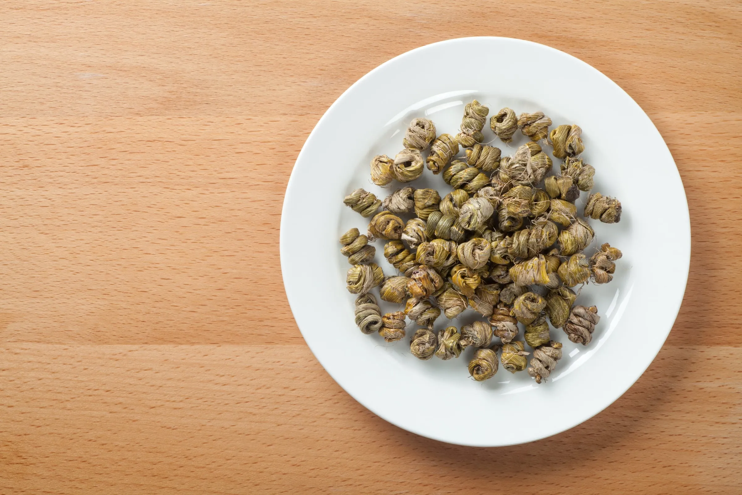 White plate of dried, coiled dendrobium on a wooden table