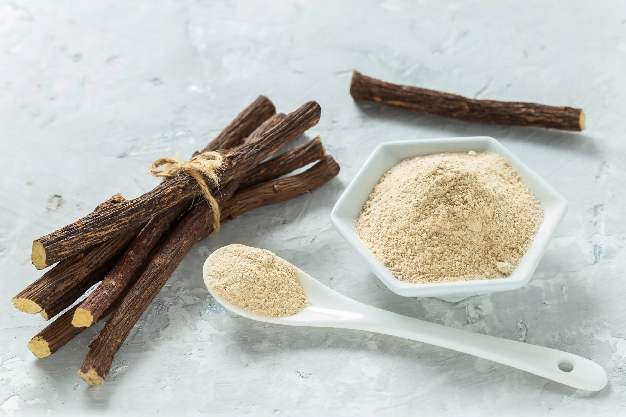 Dried Chinese licorice root sticks tied with twine beside a dish of licorice powder