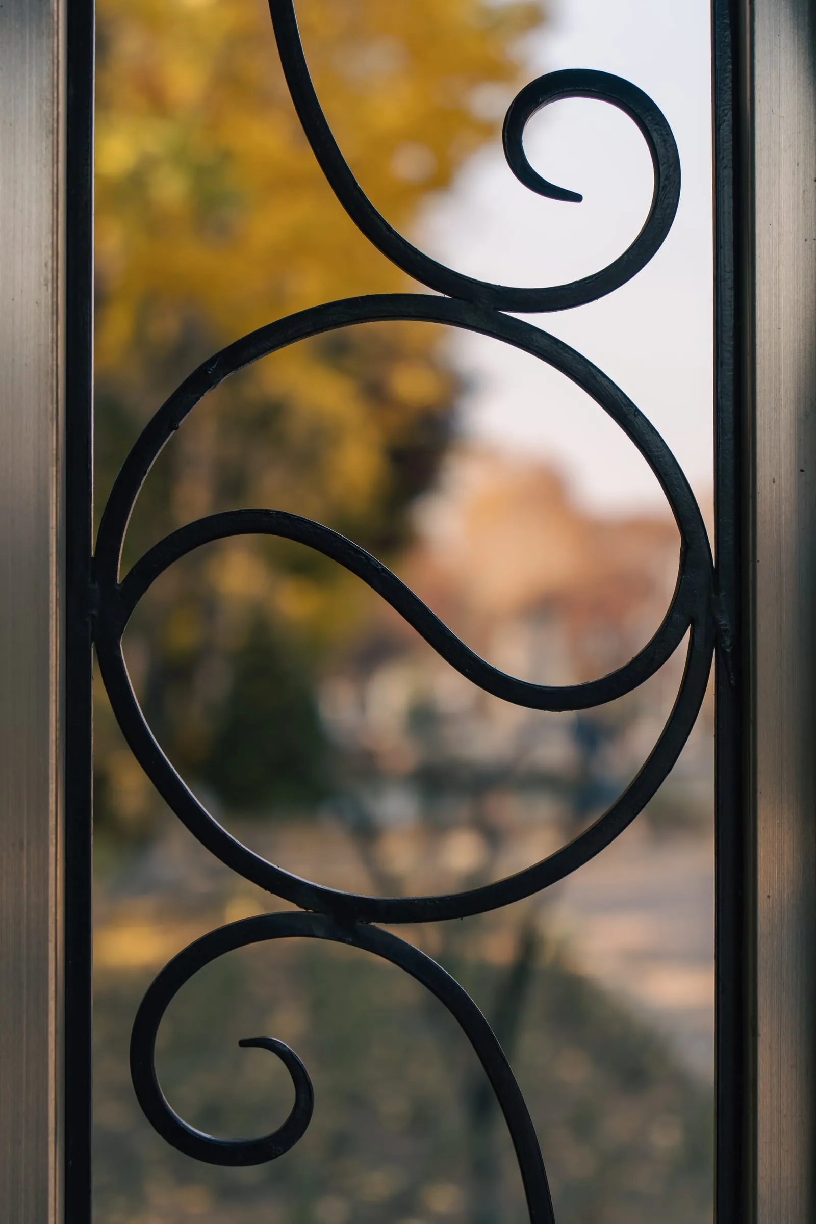 Ornate black wrought-iron gate opening onto autumn trees