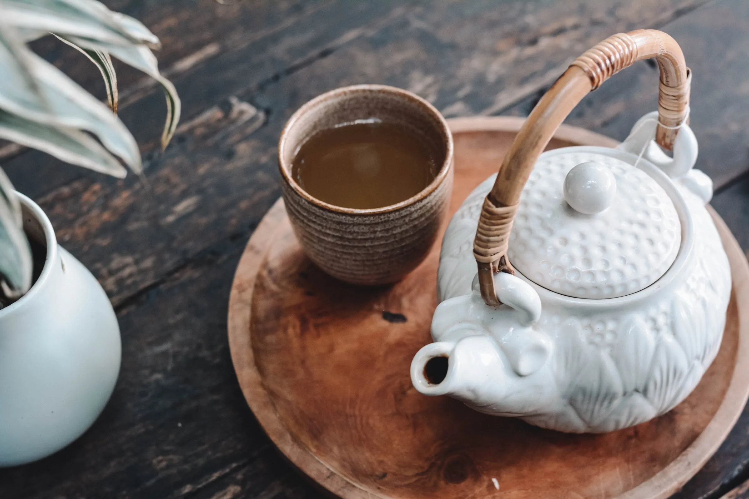 A cup of herbal tea beside a white teapot on a wooden tray